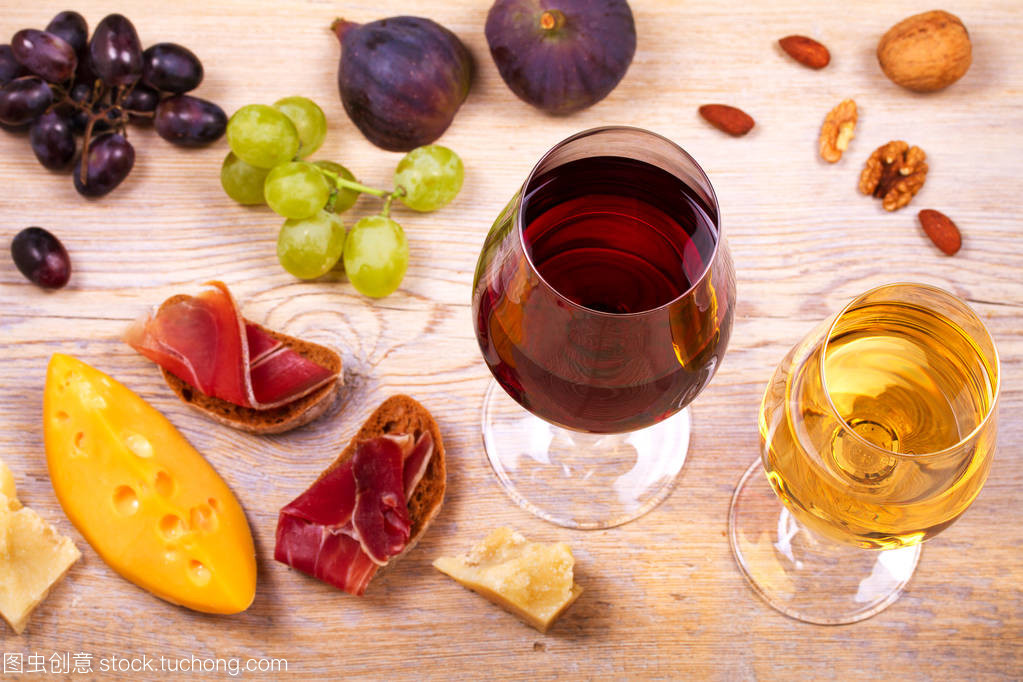 紅色和白色奶酪、 火腿、 無花果和葡萄與葡萄酒杯。木制的桌子上的酒杯。葡萄酒的靜物